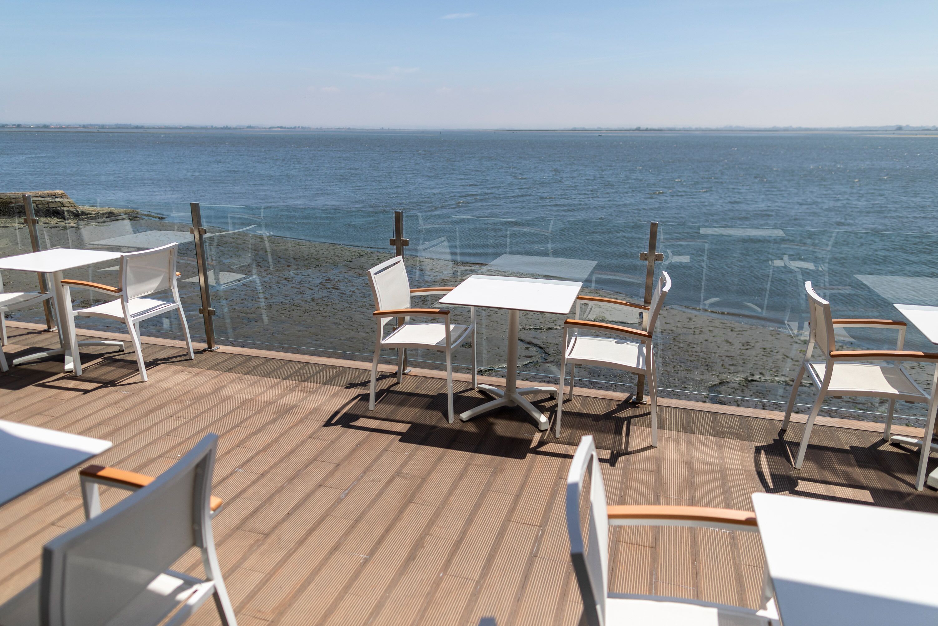 Eine Terrasse mit Tischen und Stühlen mit Blick auf ein Gewässer.