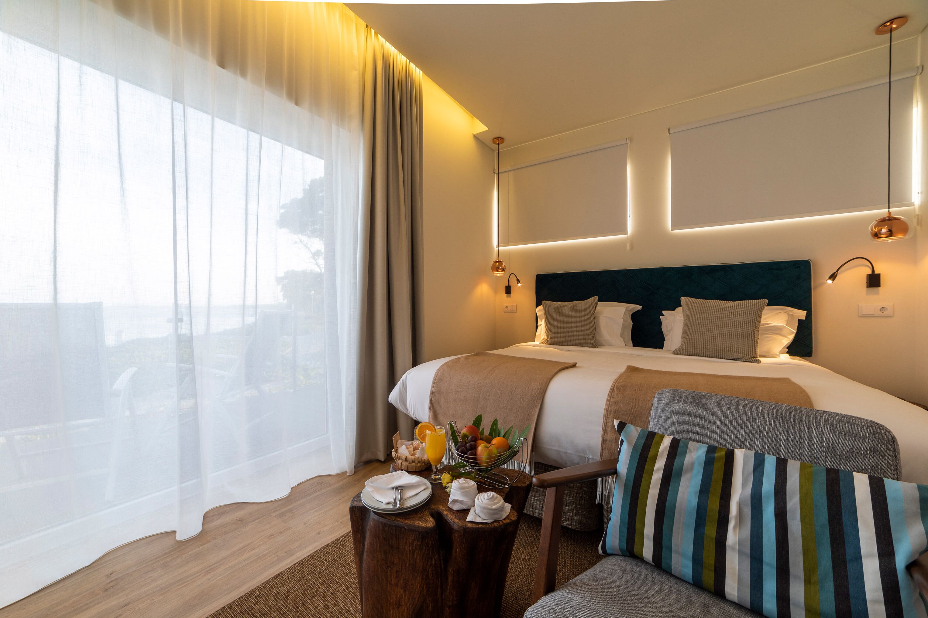 Una camera d'albergo moderna con un letto grande, comodini con accessori e vista attraverso tende leggere.