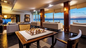 A spacious lounge with a large chess table, comfortable seating, and a view of the sea.