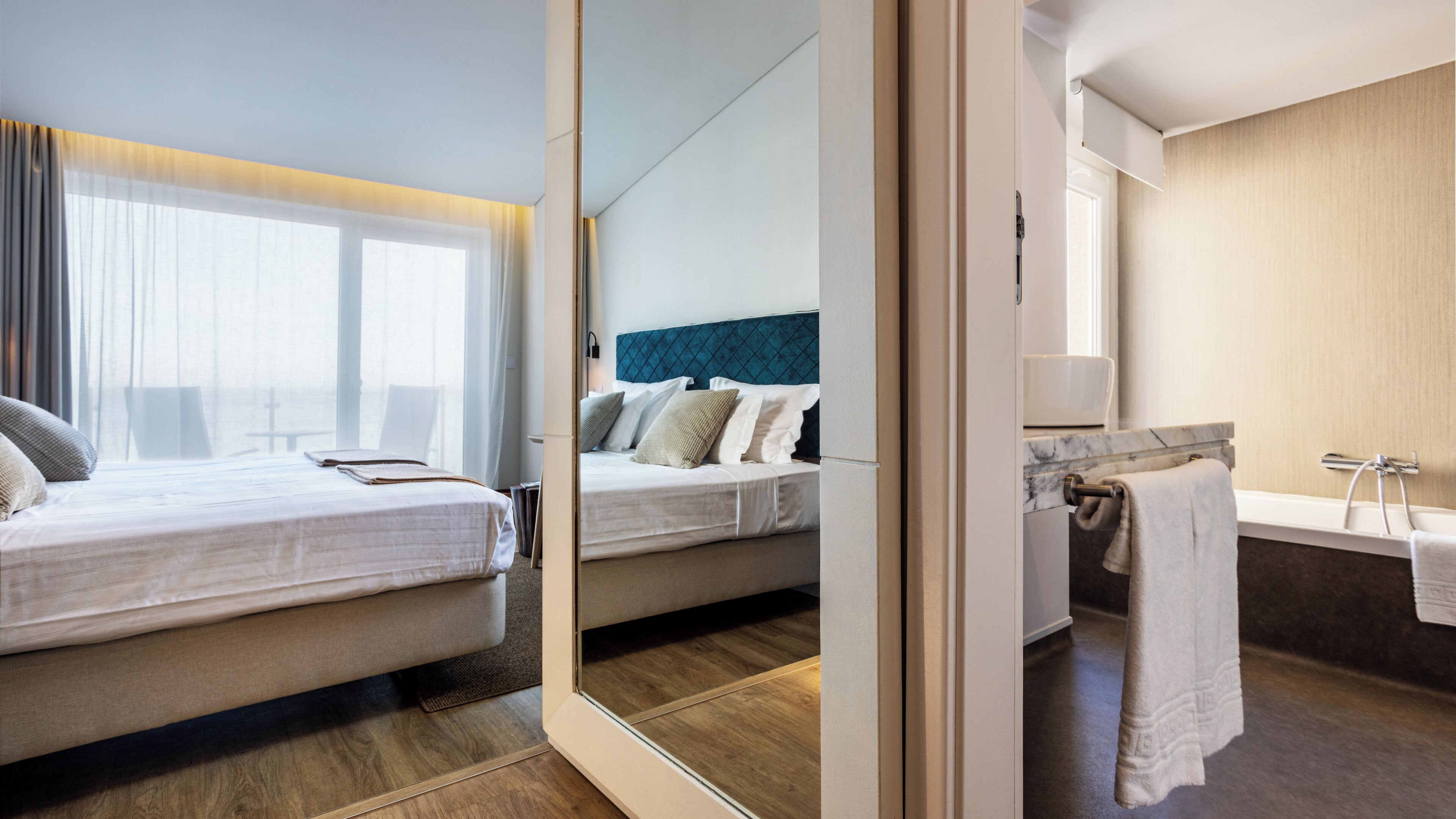 A hotel room with a bed, a bathroom with a bathtub, and a large mirror.