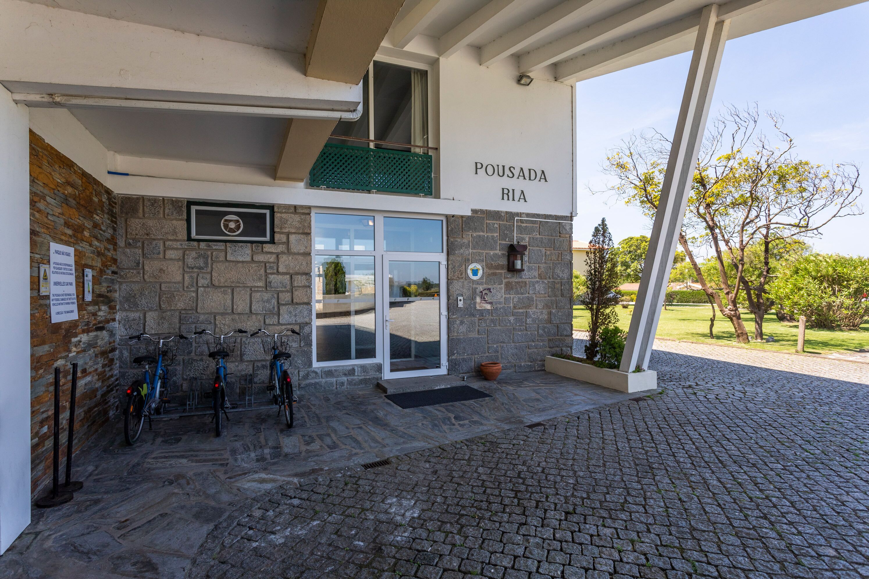 Un bâtiment à la façade en pierre, une enseigne indiquant « POUSADA RIA », et une entrée couverte avec un espace pour garer les vélos.