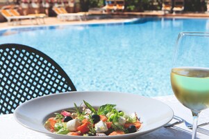 Un tavolo da pranzo con un'insalata e un bicchiere di vino bianco vicino a una piscina.