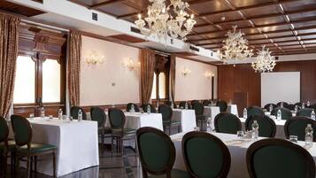 Una sala conferenze con tavoli multipli, poltrone rivestite in verde e lampadari decorati.