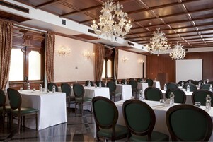 A conference room with multiple tables, green upholstered chairs, and ornate chandeliers.
