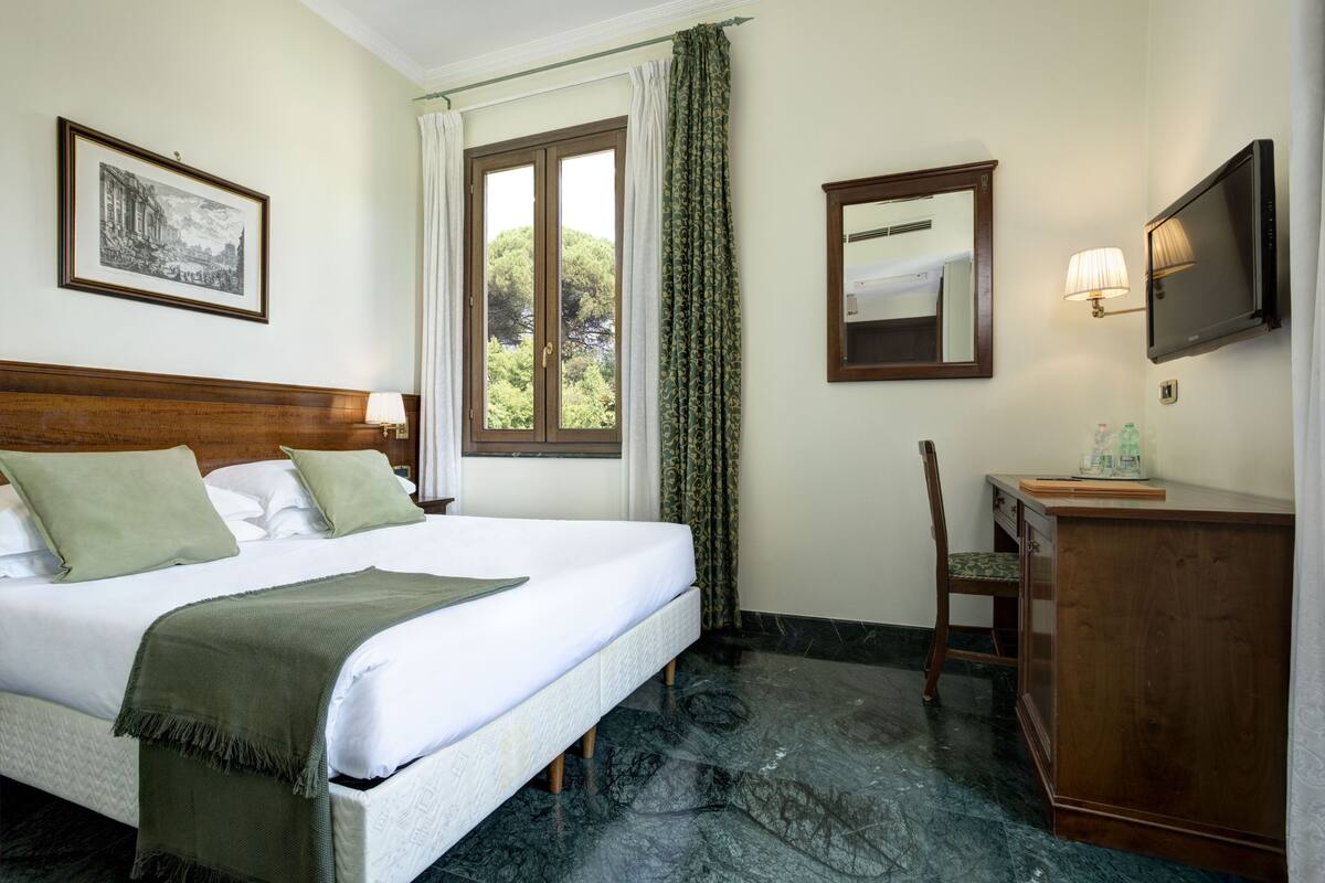 A hotel room with a bed, a desk, a chair, a television, and a window with curtains.