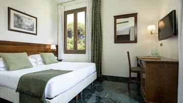 Habitación de hotel con cama, escritorio, silla, televisor y ventana con cortinas.