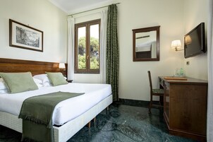 A hotel room with a bed, a desk, a chair, a television, and a window with curtains.