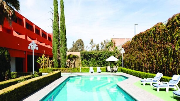 A swimming pool with lounge chairs and a red building in the background. - Hotel Misión Aguascalientes Zona Sur (Aguascalientes)