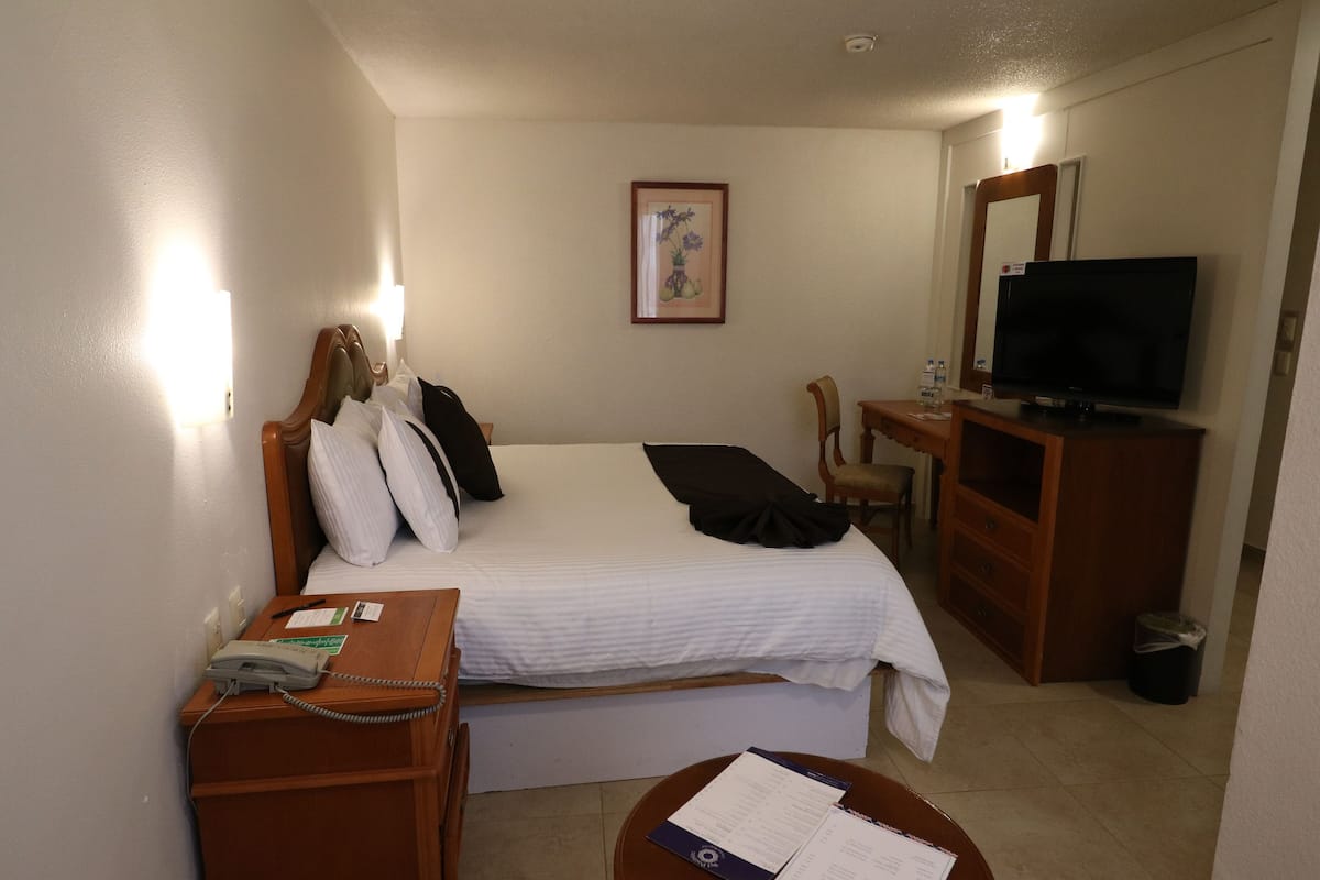 A hotel room with a bed, a desk, a chair, a television, and a telephone.
