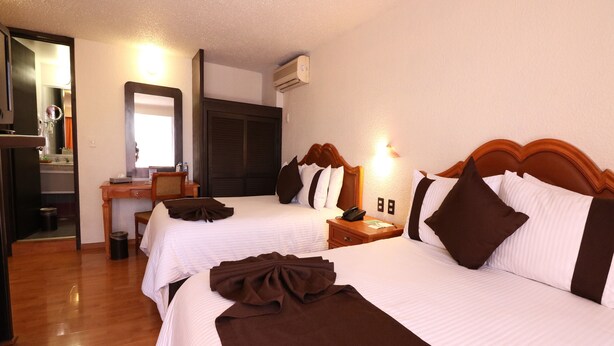 A hotel room with two beds, a desk, a chair, a mirror, and an air conditioning unit. - Hotel Misión Aguascalientes Zona Sur (Aguascalientes)