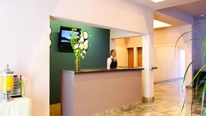A reception area with a counter, a television mounted on the wall, and a vase with flowers. - Hotel Misión Aguascalientes Zona Sur (Aguascalientes)