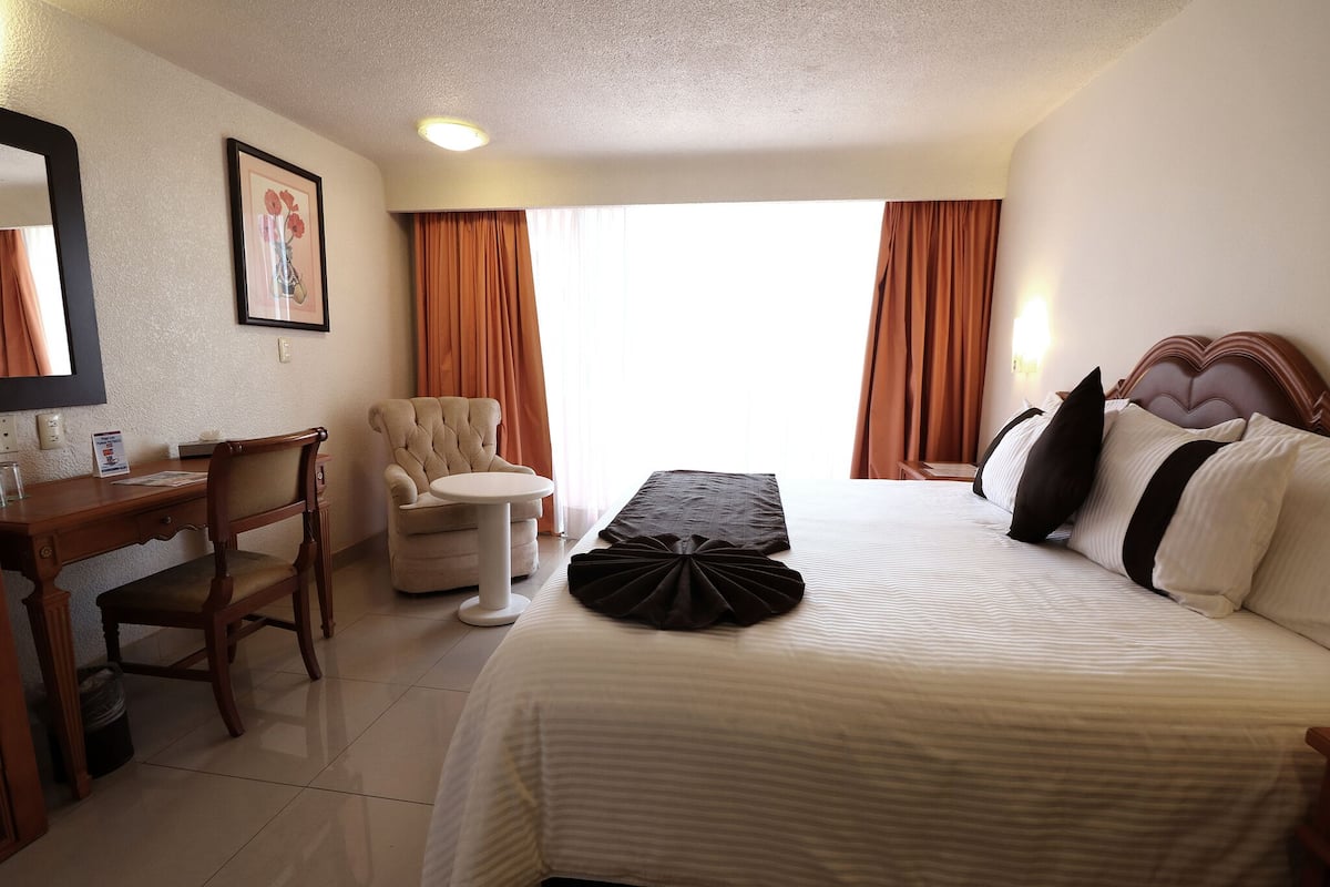 A hotel room with a bed, a desk, a chair, and a small table.