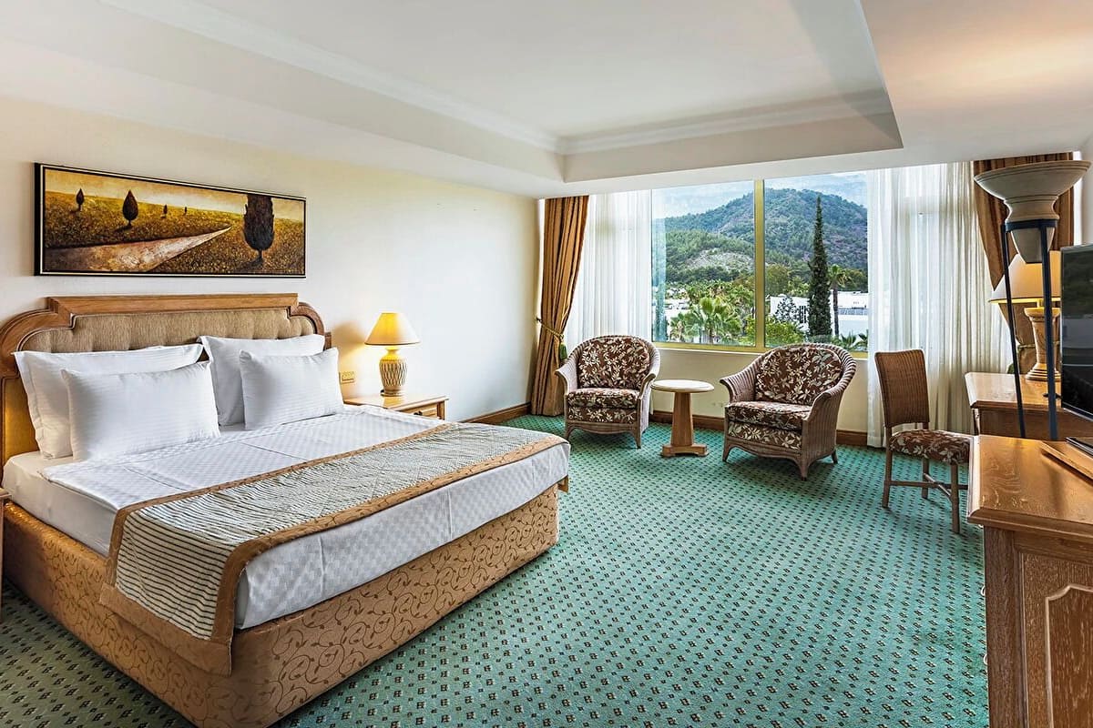 Habitación de hotel con una cama grande, dos sillones, una mesita, un televisor y un cuadro en la pared.