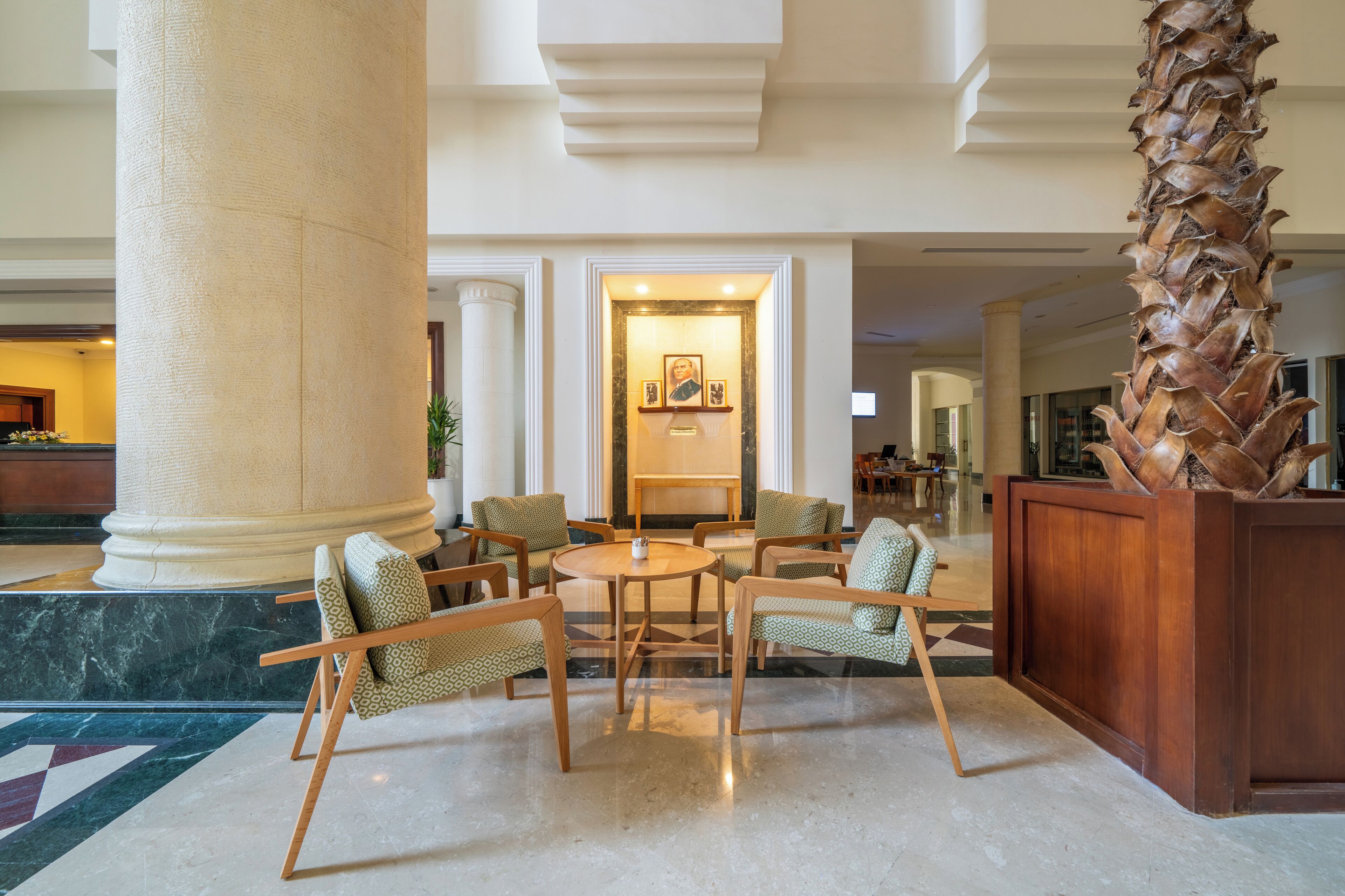 Un vestíbulo con una columna imponente, una recepción y una zona de estar con sillas y una mesa.