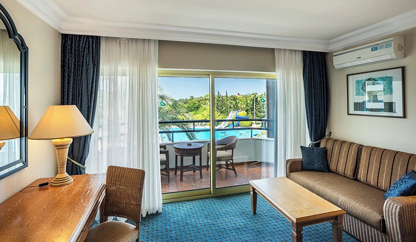 A hotel room with a balcony, a sofa, a table, and a lamp.