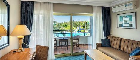 A hotel room with a balcony, a sofa, a table, and a lamp.
