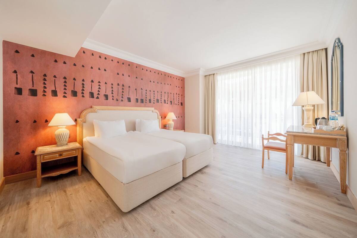 Una habitación de hotel con cama, dos mesitas de noche con lámparas, un escritorio y una silla.
