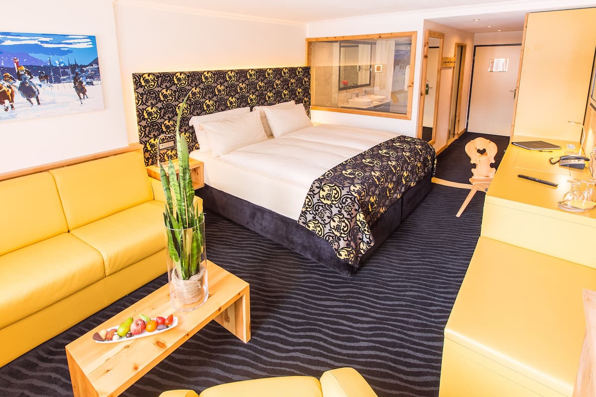 Ein Hotelzimmer mit Bett, einer Couch, einem kleinen Tisch mit Früchten, einer Pflanze und einem Spiegel.