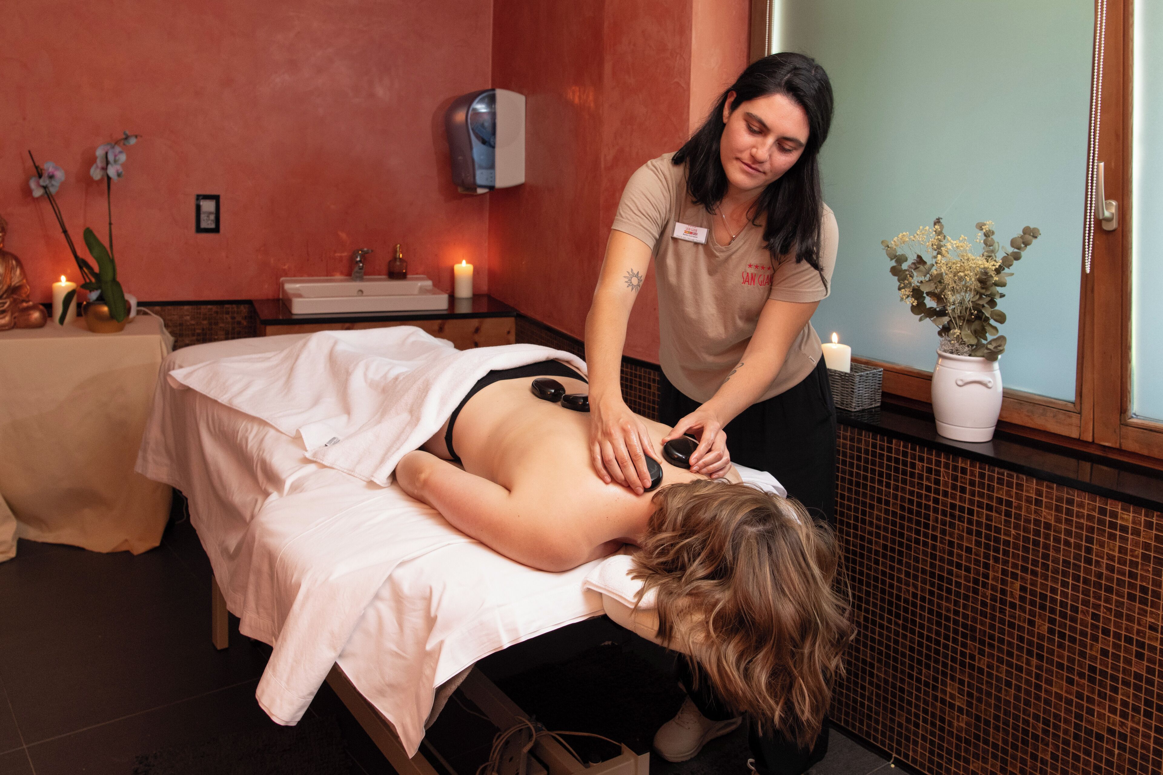 Une séance de massage dans une pièce dont un mur est recouvert de carreaux, avec un petit autel orné de bougies et un vase contenant des fleurs séchées.