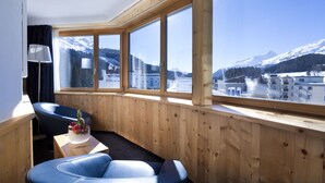 Quarto com grande janela com vista para a montanha, interior em madeira e uma pequena mesa com objeto decorativo.