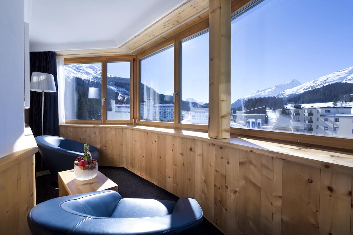 Ein Zimmer mit großem Fenster und Blick auf die Berge, Holzvertäfelung und einem kleinen Tisch mit einem dekorativen Gegenstand.