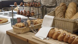 Um buffet com diversos pães e doces, incluindo uma montra de doces em três níveis e cestas de pão.