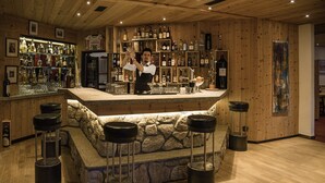 Uma área de bar com um bartender, bancos de pedra e vários banquinhos.