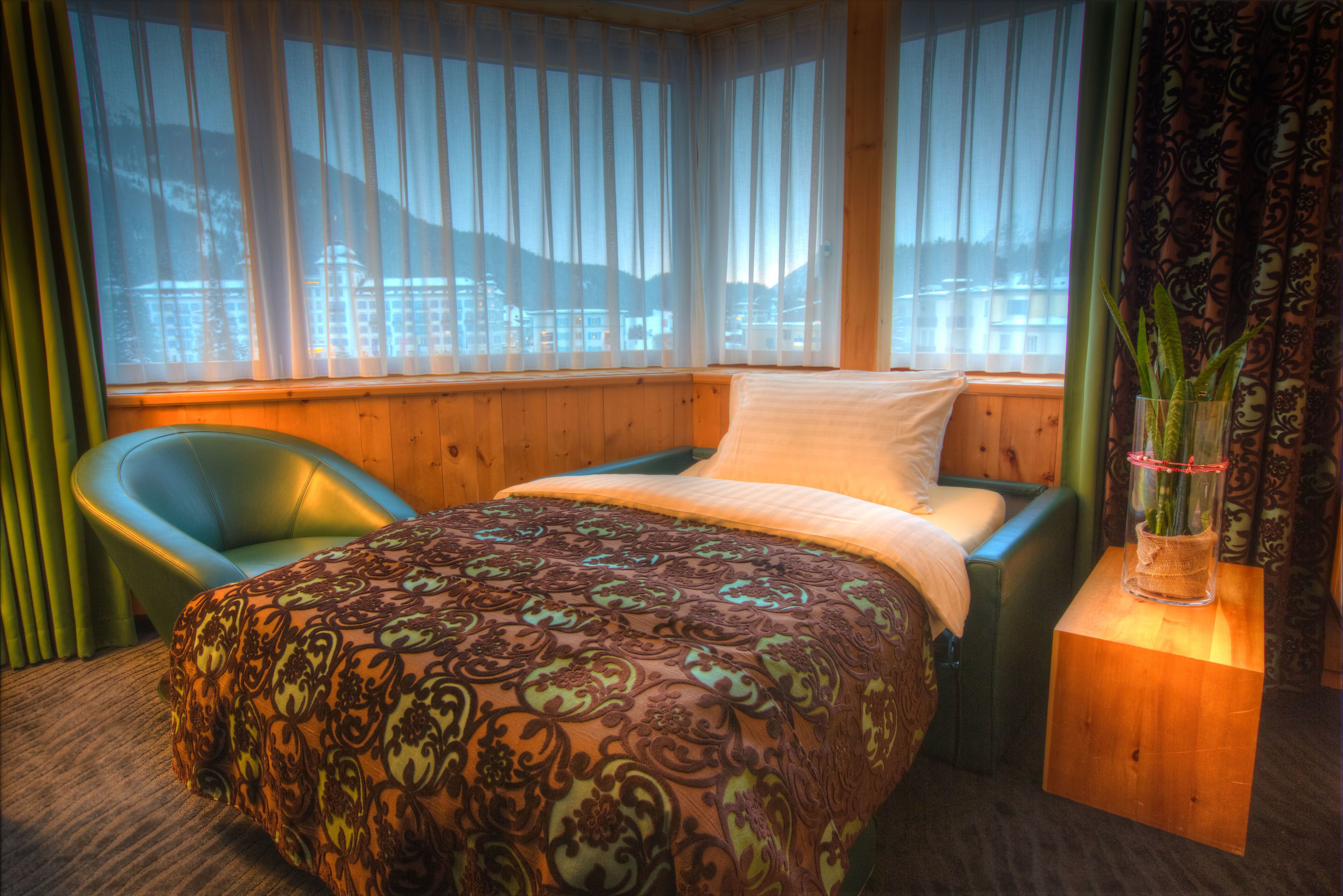 A hotel room with a bed, a chair, and a nightstand with a vase.