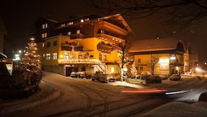A multi-story hotel with a snow-covered street in front, illuminated by warm interior lights. - Hotel Gasthof zum Kirchenwirt (Puch bei Hallein)