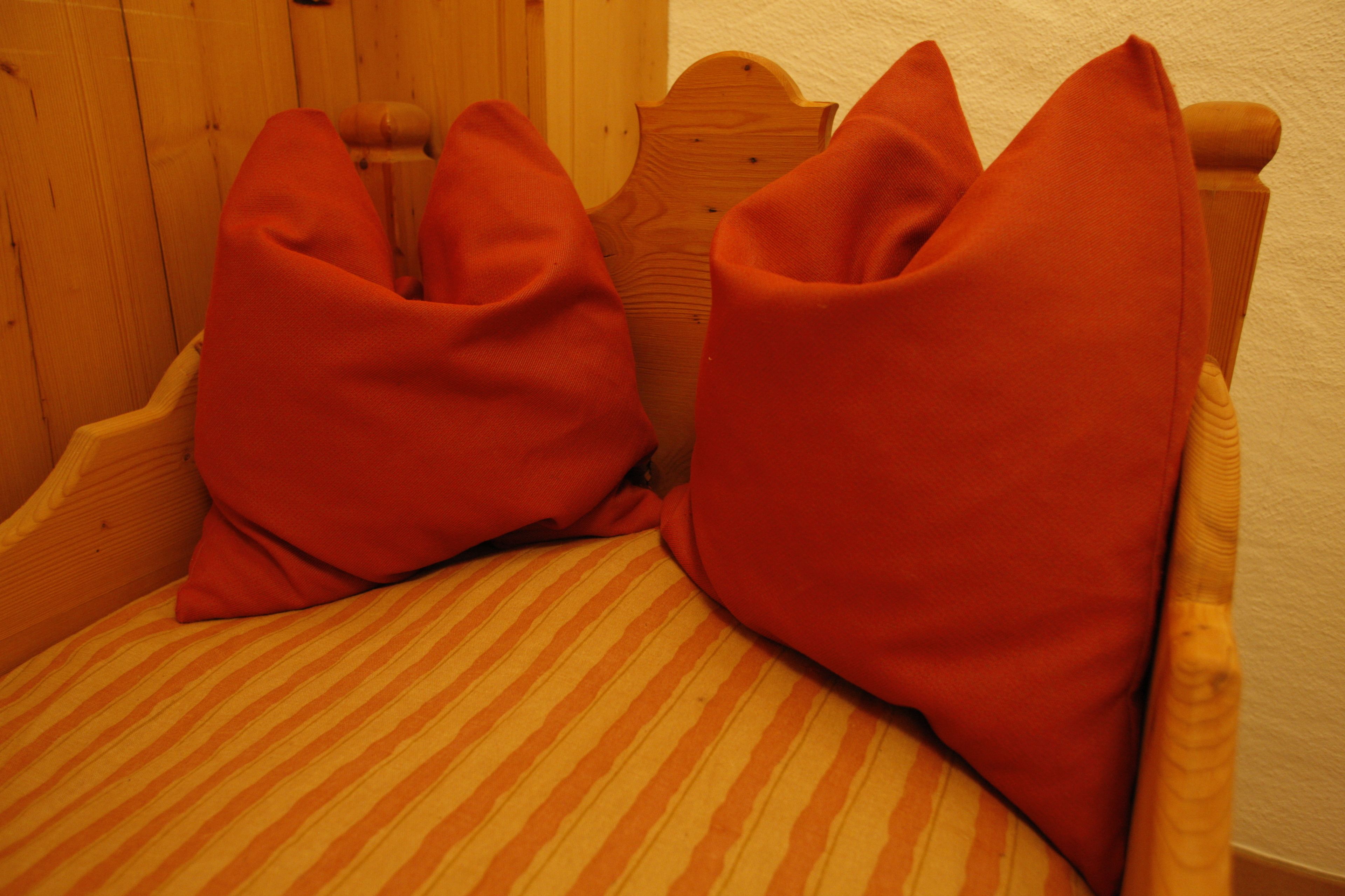 Une chaise en bois avec un coussin à rayures et deux oreillers rouges.