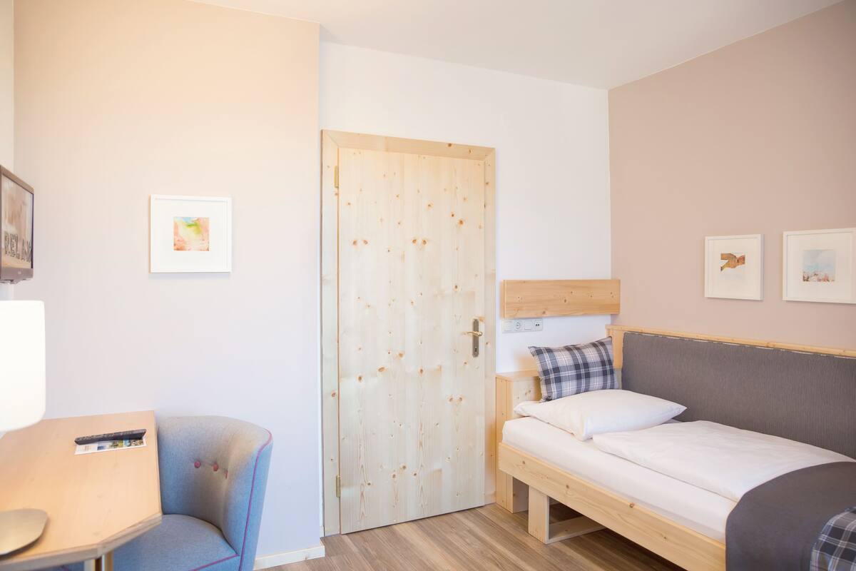 A bedroom with a wooden bed, a small chair, a desk, and a door.