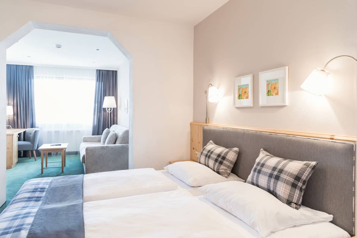 A hotel room with two beds, a desk, a chair, and a large window with curtains.