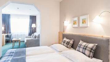A hotel room with two beds, a desk, a chair, and a large window with curtains.