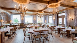 A large dining hall with wooden tables and chairs, chandeliers, and large windows. - Hotel Gasthof zum Kirchenwirt (Puch bei Hallein)