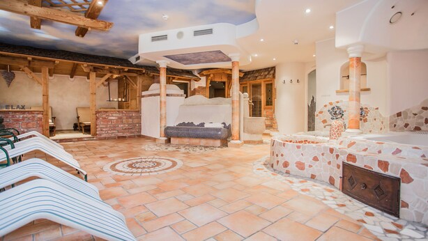 A spa area with a stone floor, wooden beams, and a seating area with a massage table. - Hotel Gasthof zum Kirchenwirt (Puch bei Hallein)