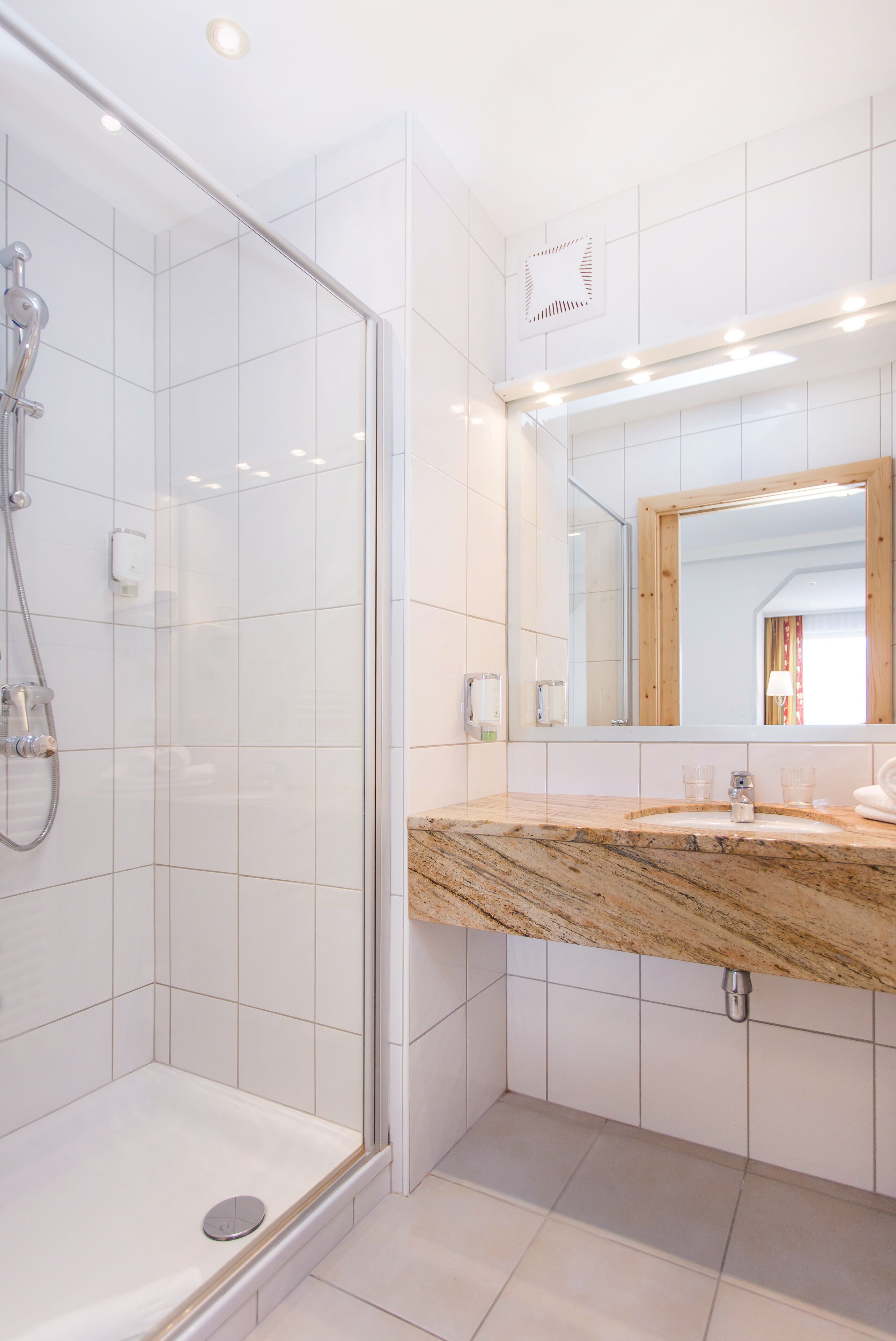 A modern bathroom with a glass-enclosed shower, a marble countertop, and a large mirror.