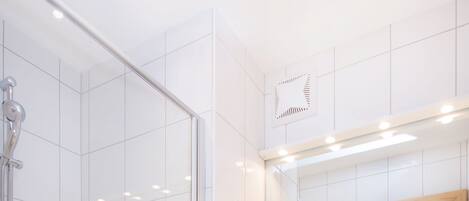 A modern bathroom with a glass-enclosed shower, a marble countertop, and a large mirror.