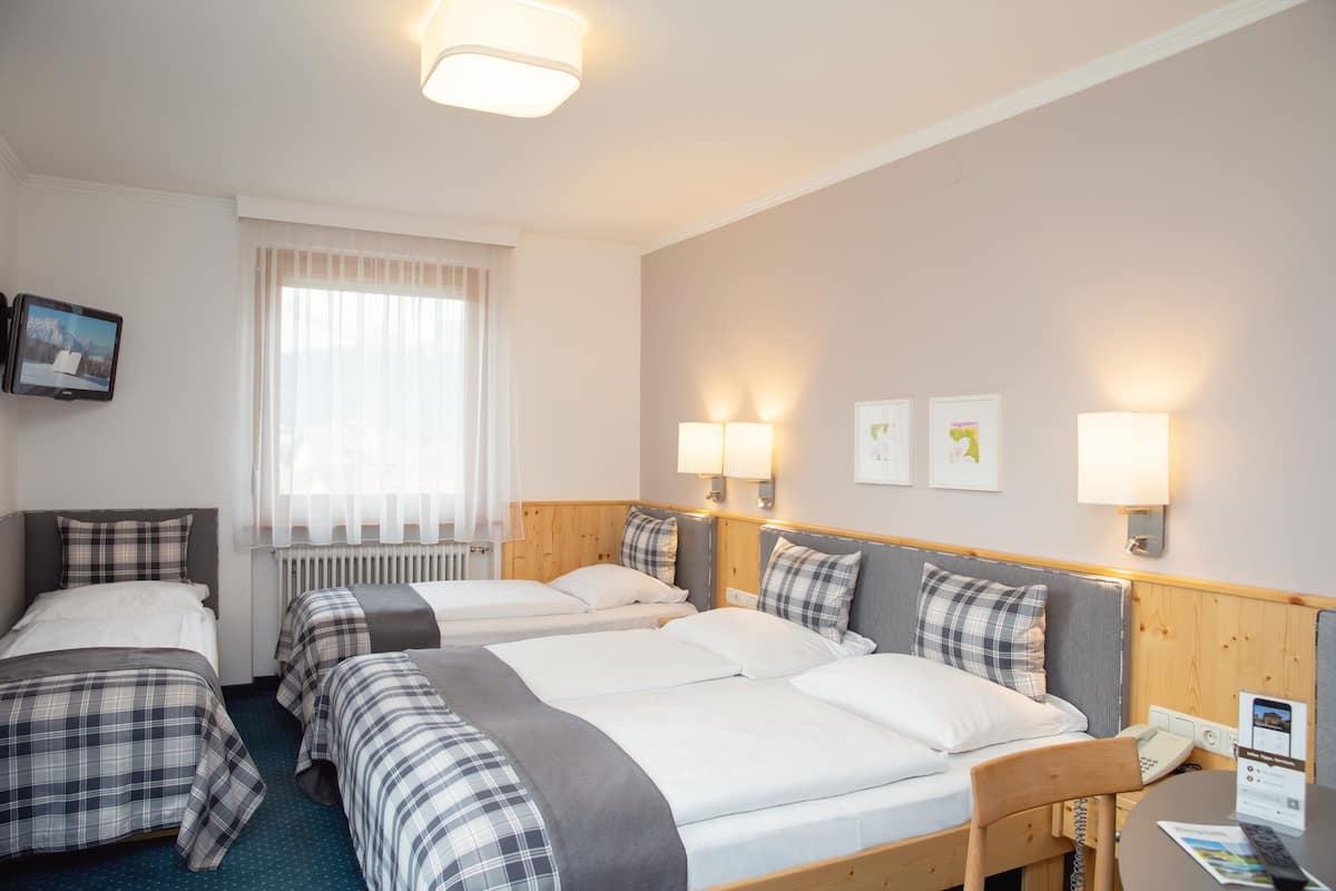 A hotel room with two beds, a desk, a chair, a TV, and a window with curtains.