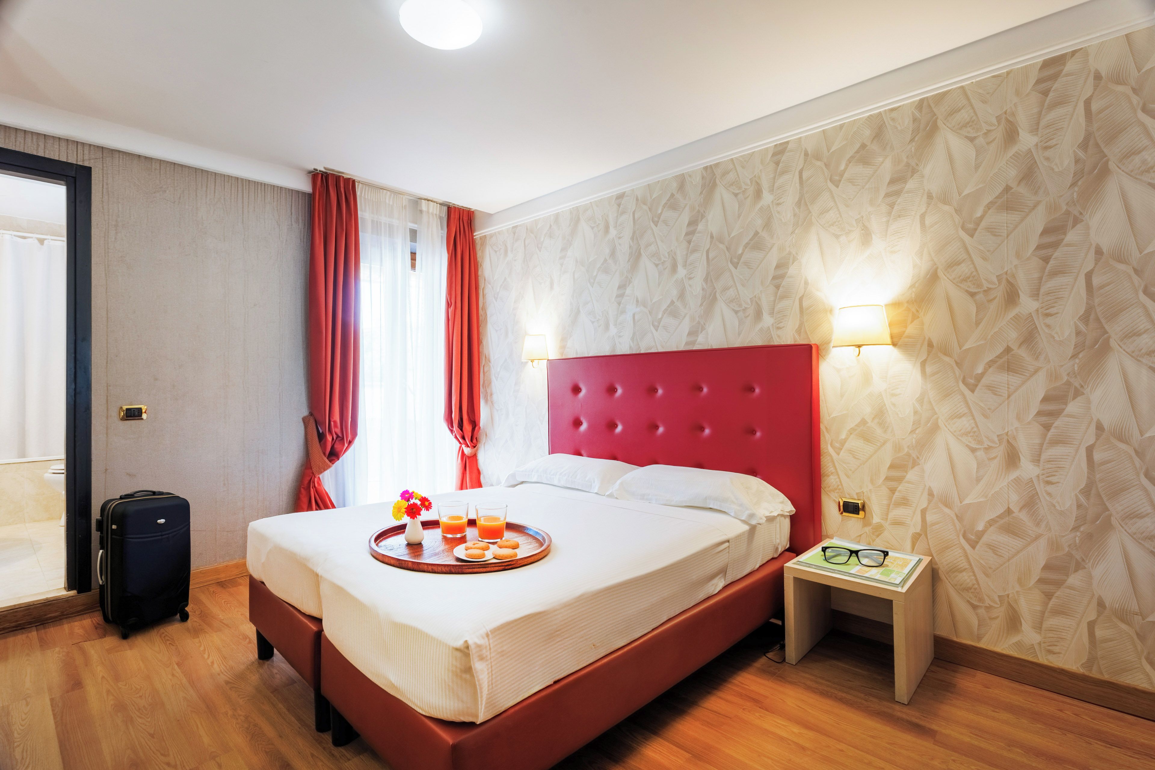 A hotel room with a bed, bedside table, and a suitcase.