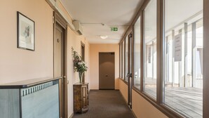 A hotel corridor with framed artwork, a vase with flowers, and a view of the outside balcony. - Hotel Villa Rosa (Rome)