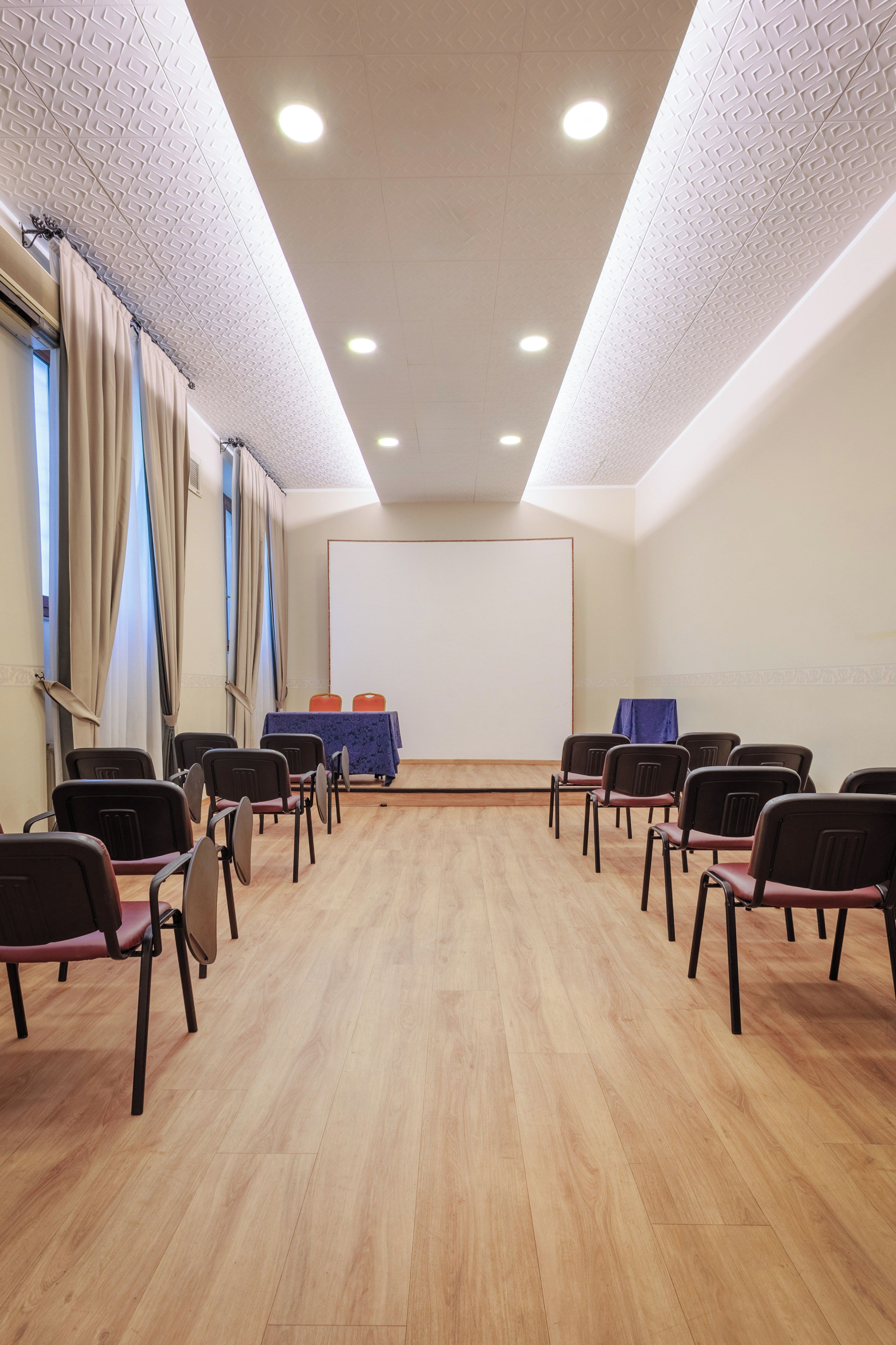 A conference room with a stage, rows of chairs, and a projector screen.