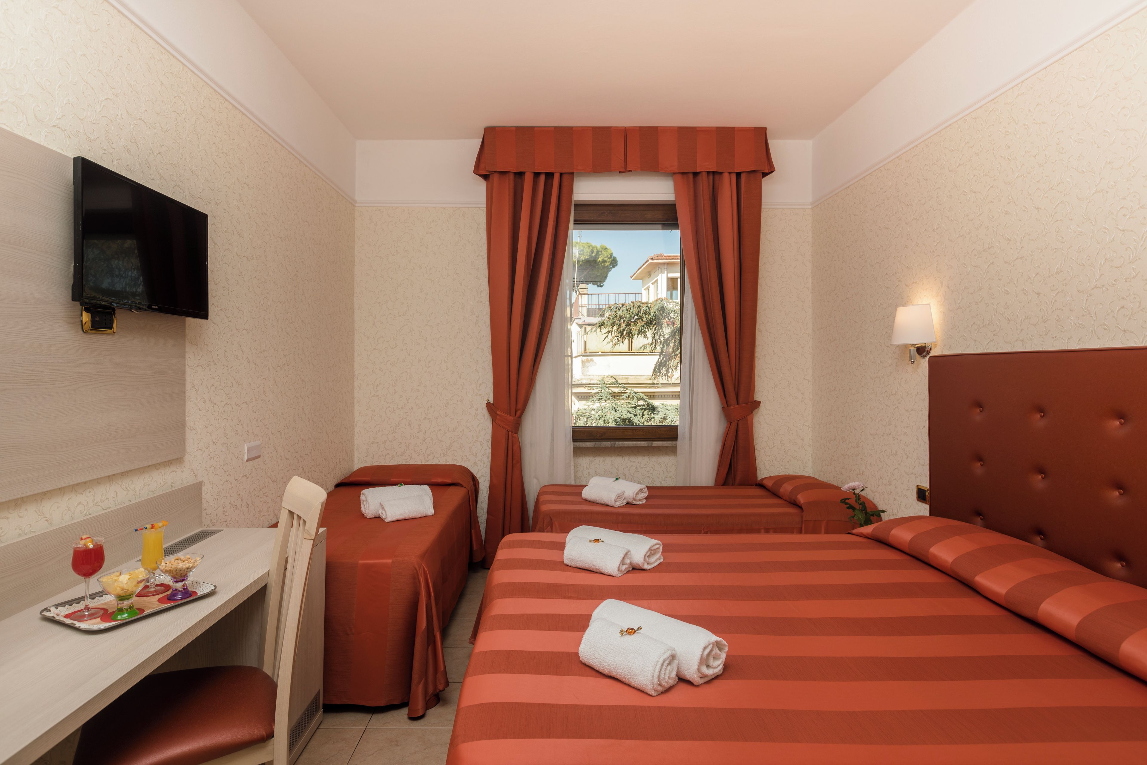 A hotel room with two beds, a desk, a television, and a window with curtains.