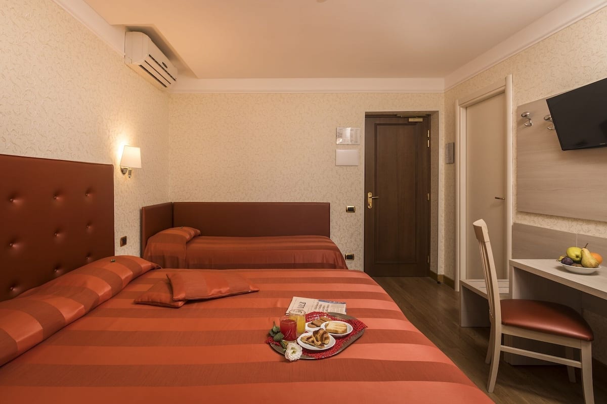A hotel room with two beds, a desk with a chair, a television, and a breakfast tray on the bed.