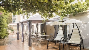 An outdoor patio with tables and chairs, covered by umbrellas, and surrounded by greenery. - Hotel Villa Rosa (Rome)