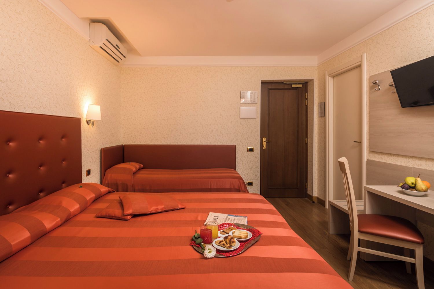 Una habitación de hotel con una cama grande, un escritorio con una silla, un televisor y una puerta.
