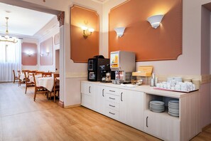 A hotel room with a breakfast bar, coffee machine, and a dining area with a table and chairs.