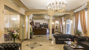 A spacious lobby with a grand chandelier, leather sofas, a reception desk, and a decorative floor pattern. - Hotel Villa Rosa (Rome)