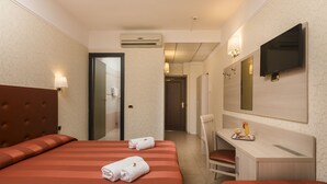 A hotel room with two beds, a desk, a chair, a TV, and an air conditioning unit. - Hotel Villa Rosa (Rome)