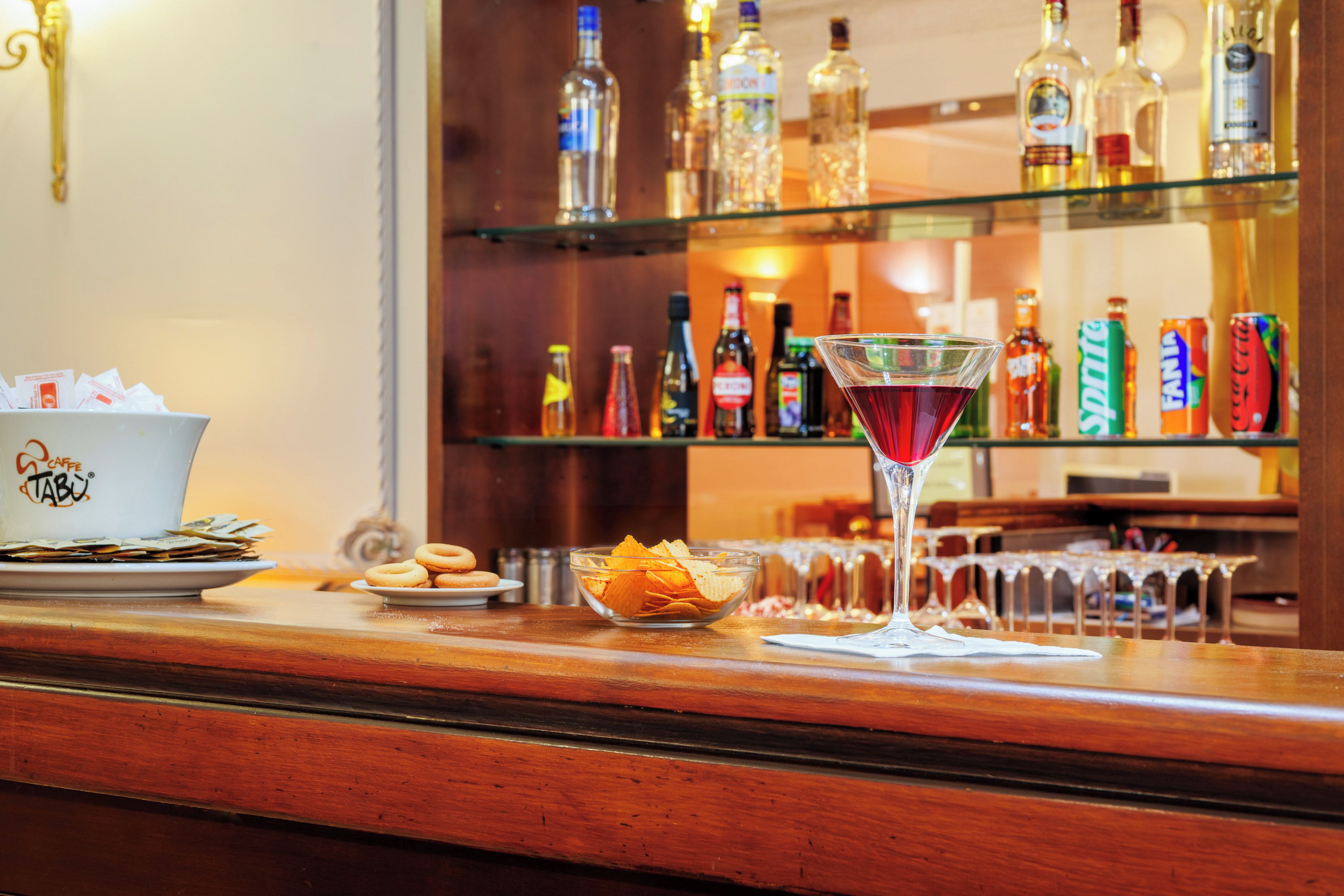 A bar area with a martini glass, snacks, and a variety of bottles on shelves.