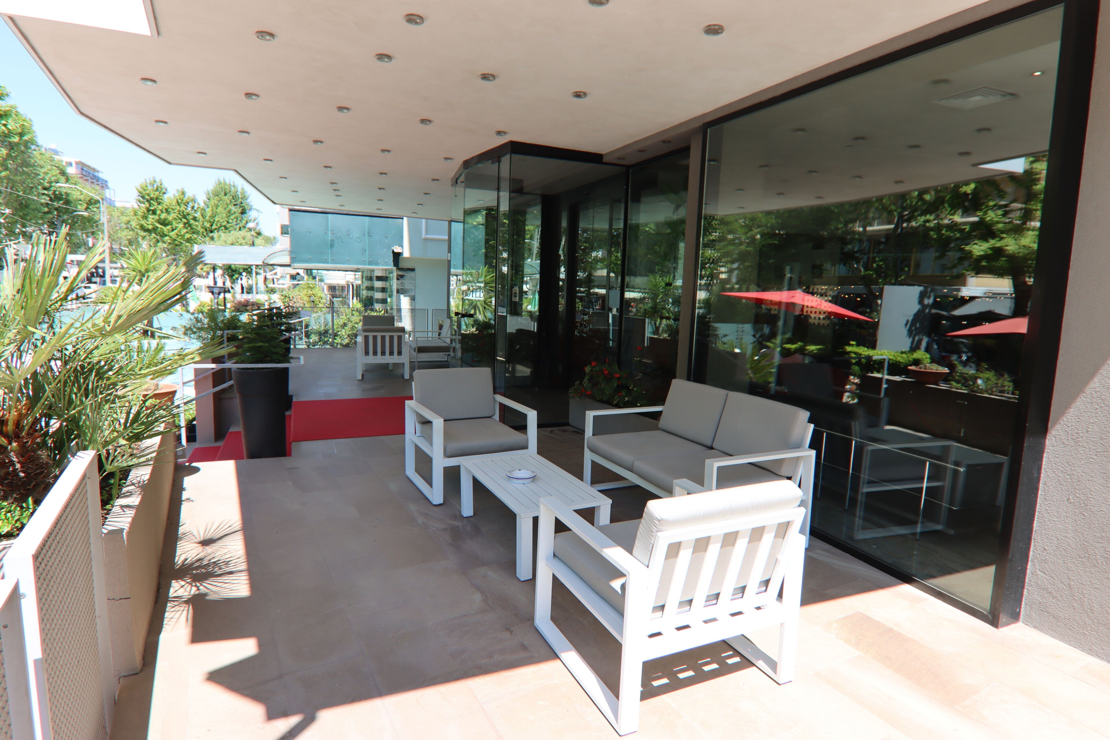 Un patio exterior con mobiliario blanco, un muro de cristal y vistas del entorno.